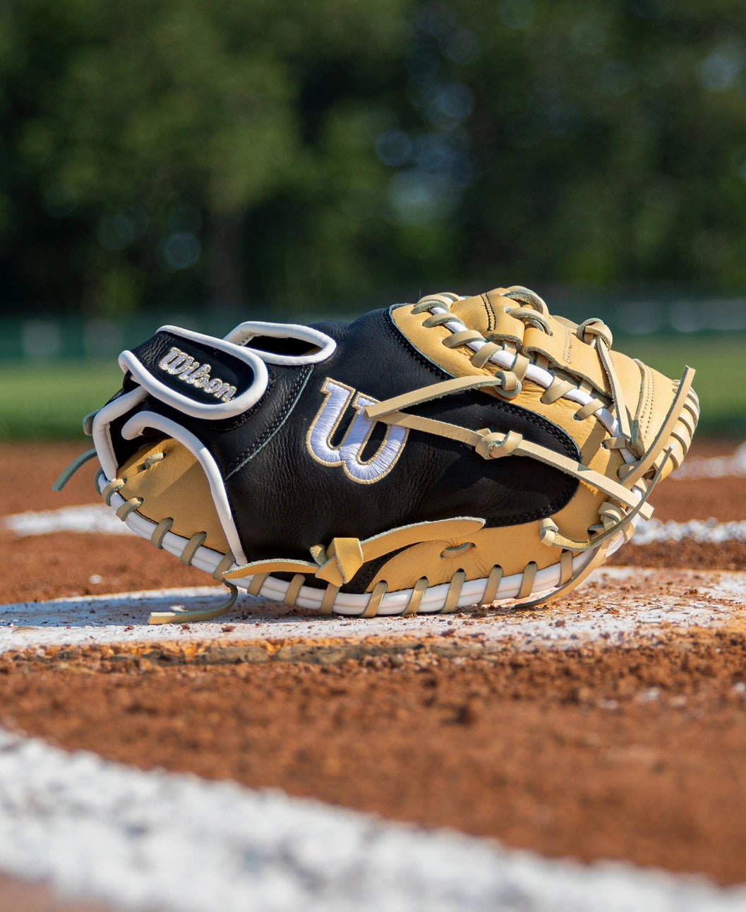 A black and tan Wilson A700 32.5″ Baseball Catcher’s Mitt: WBG04701RT325 sitting on a dirt field base line.