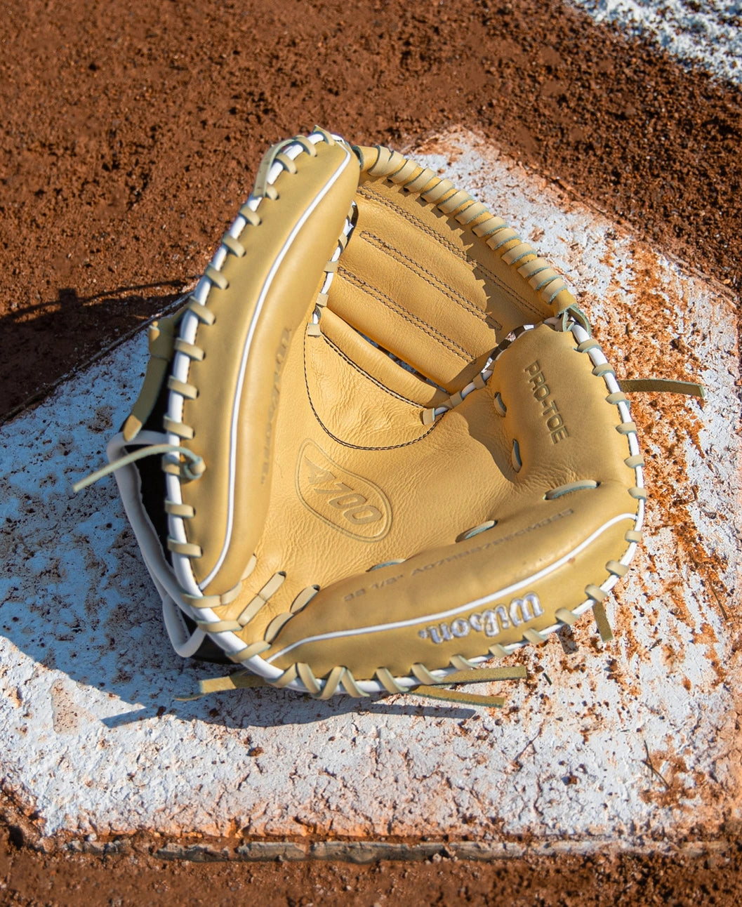 Wilson A700 32.5″ Baseball Catcher’s Mitt: WBG04701RT325 made of tan leather resting on a white base on a dirt infield.