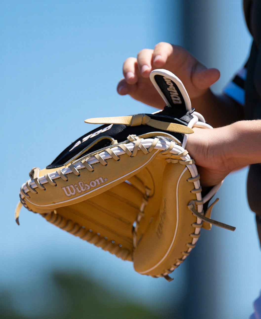 A player adjusting a tan and black Wilson A700 32.5″ Baseball Catcher’s Mitt: WBG04701RT325.