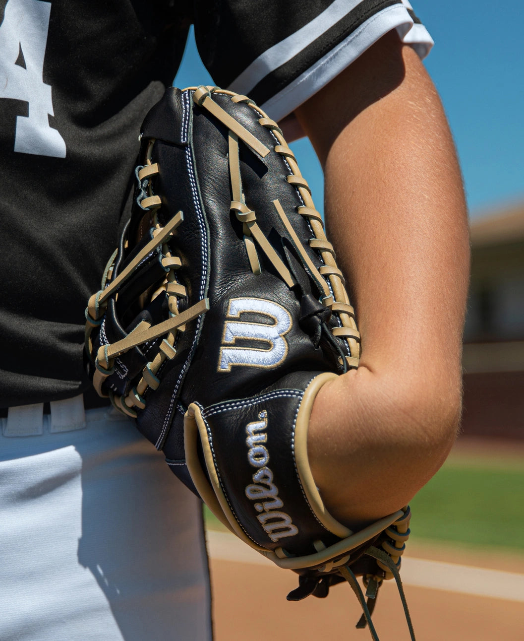 A player holds a black Wilson A700 12″ Baseball First Base Mitt: WBG04801RT1620 with tan lacing against their side.