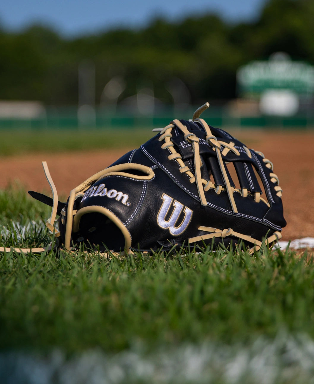 A black and tan Wilson A700 12″ Baseball First Base Mitt: WBG04801RT1620 resting on a grassy field.