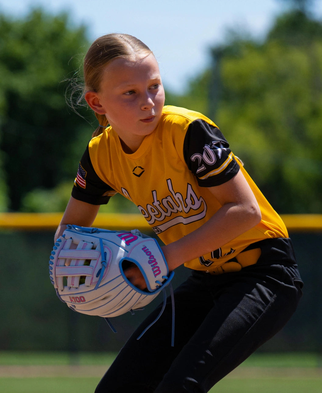 A young softball player in a yellow jersey wearing a white and light blue Wilson A700 12″ Fastpitch Glove: WBG04901RT12 while preparing to catch.