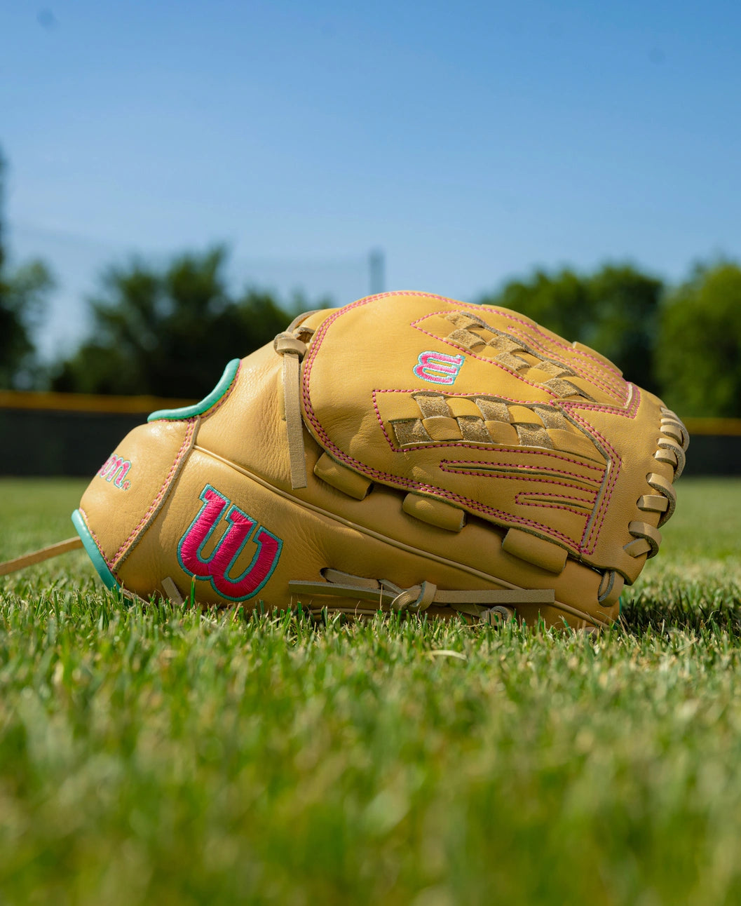 Wilson A700 12.5″ Fastpitch Glove: WBG05001RT125 with tan leather, pink and teal embroidered logos, resting on a grassy field.