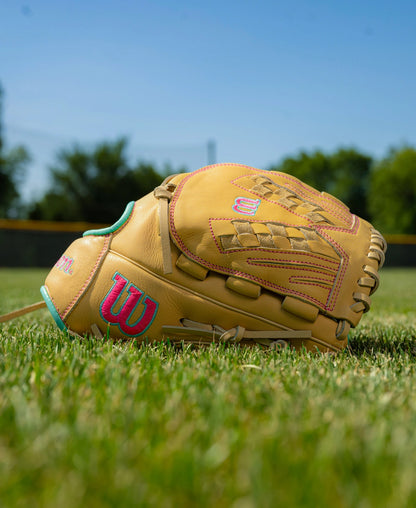 Wilson A700 12.5″ Fastpitch Glove: WBG05001RT125 with tan leather, pink and teal embroidered logos, resting on a grassy field.