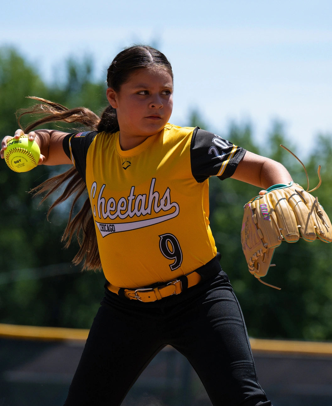A young fastpitch player in a yellow and black uniform throws a softball while wearing a tan full grain leather Wilson A700 12.5″ Fastpitch Glove: WBG05001RT125.