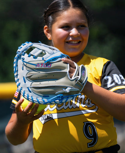 A softball player in a yellow jersey holds a grey and blue Wilson A700 33″ Fastptich Catcher’s Mitt: WBG05101RT33 containing a yellow softball.