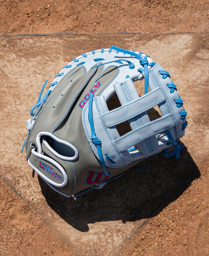 Grey and light blue full grain leather Wilson A700 33″ Fastptich Catcher’s Mitt: WBG05101RT33 with blue lacing resting on a dirt surface.