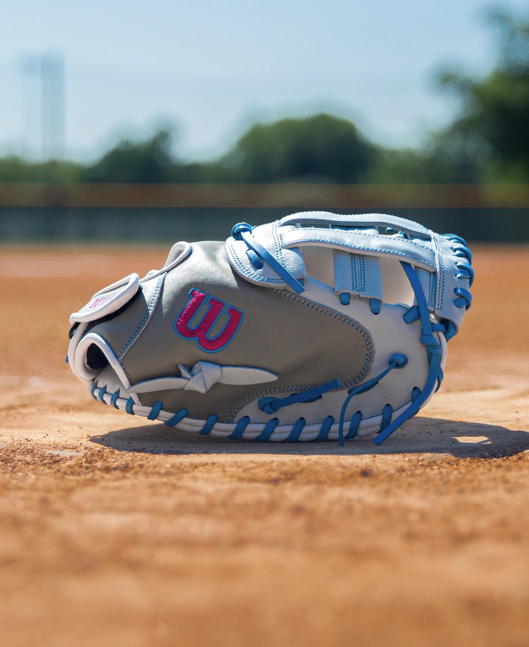 Wilson A700 33″ Fastptich Catcher’s Mitt in grey and white full grain leather with bright blue lacing sitting on a dirt field.