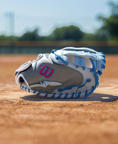 Wilson A700 33″ Fastptich Catcher’s Mitt in grey and white full grain leather with bright blue lacing sitting on a dirt field.