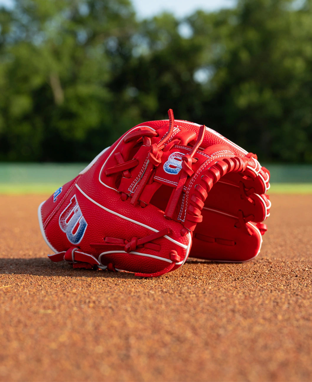 A red Wilson A1000 PF11SS 11″ Baseball Glove: WBG05201RT11 infield glove resting on the dirt surface.