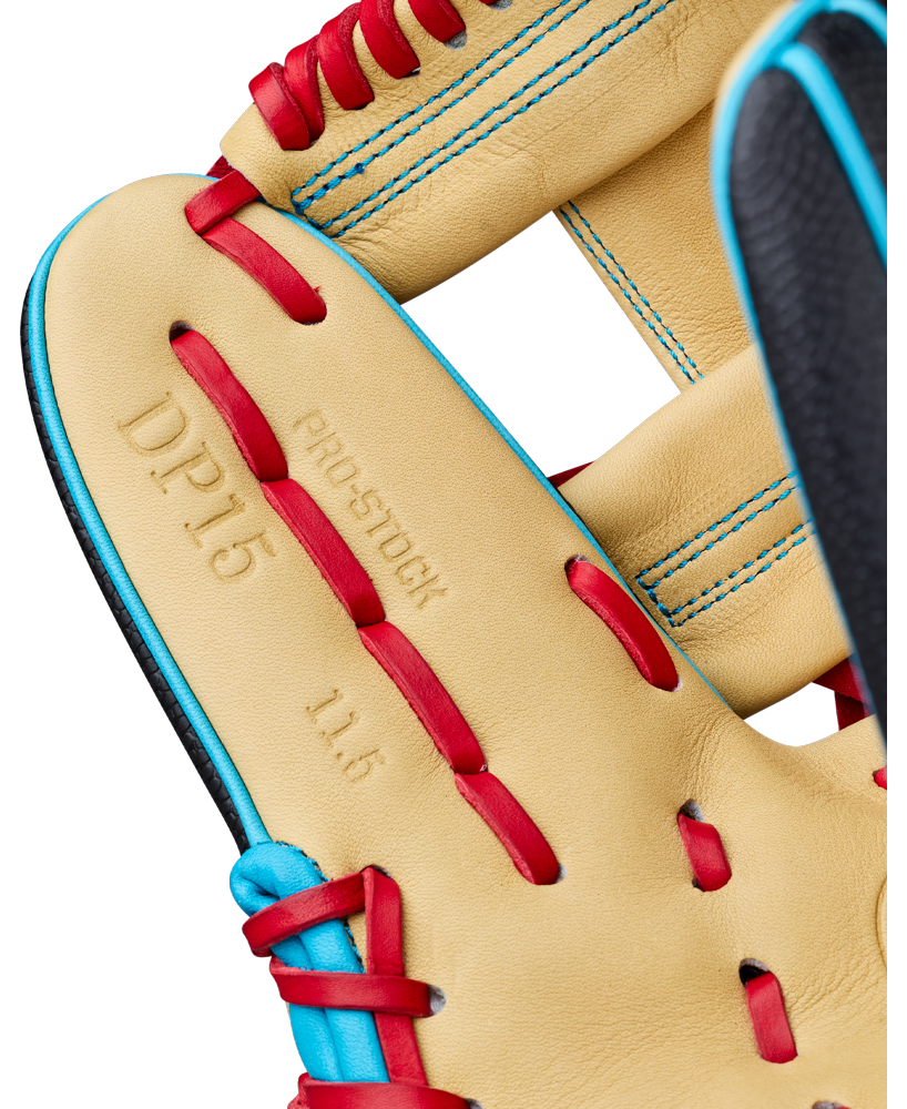 Close-up of a Wilson A2000 DP15SS 11.5″ Baseball Glove (WBG05501RT115) in tan, featuring red and blue laces, detailed blue stitching, and a portion of black leather. The glove displays embossed text “DP15,” “PRO-STOCK,” and “11.5” and showcases the Pedroia Fit design.