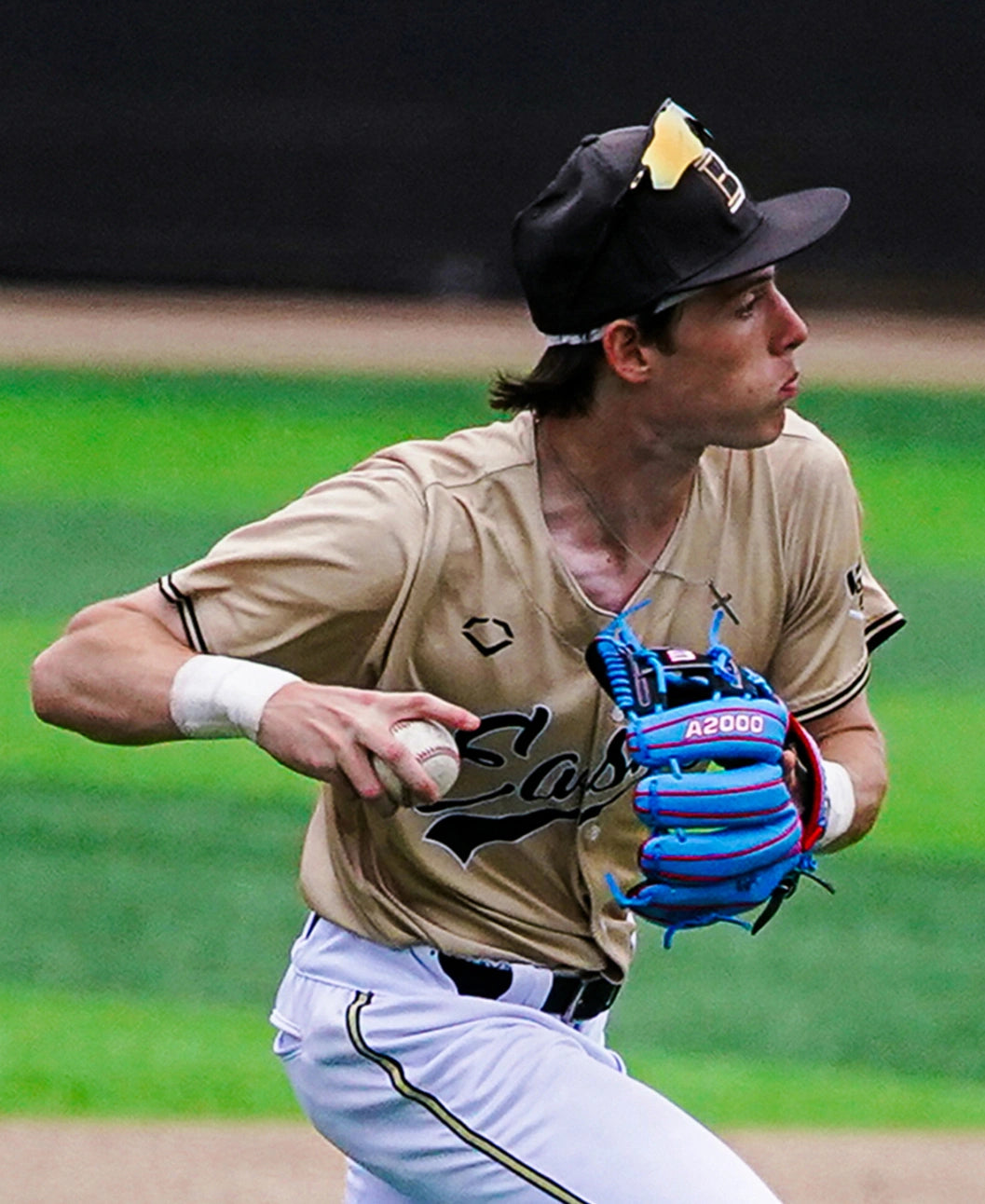 A baseball player wearing a tan jersey and black cap stands ready to throw on a green field, gripping a Wilson A2000 1786SS 11.5″ Baseball Glove (WBG05601RT115) by Wilson and focusing intently on his target.