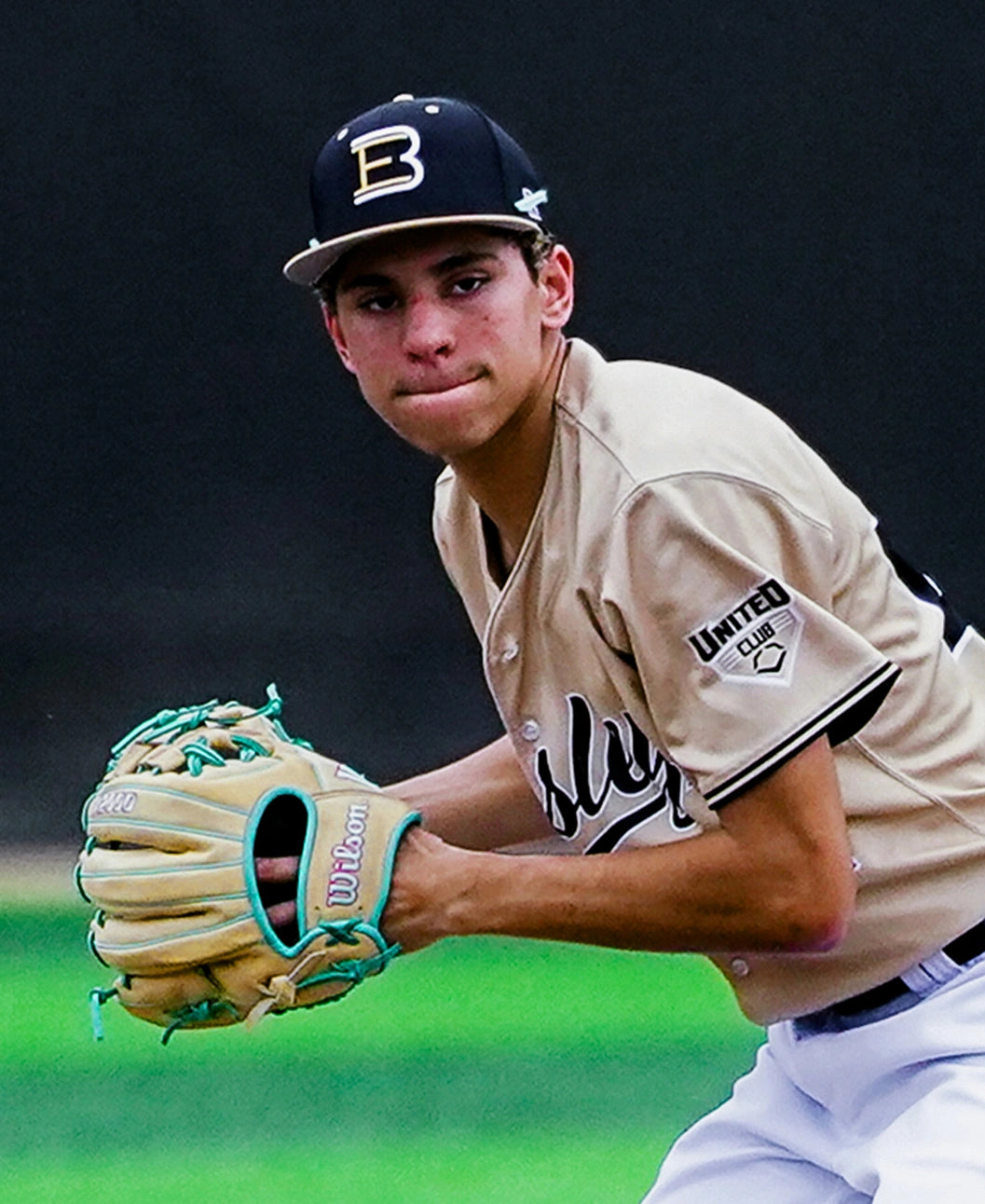A baseball player in a tan jersey and black cap gets ready to throw the ball, gripping a Wilson A2000 1975 11.75″ Baseball Glove (WBG05701RT1175) in light blue and tan, featuring an extra deep pocket, with a focused expression on his face.