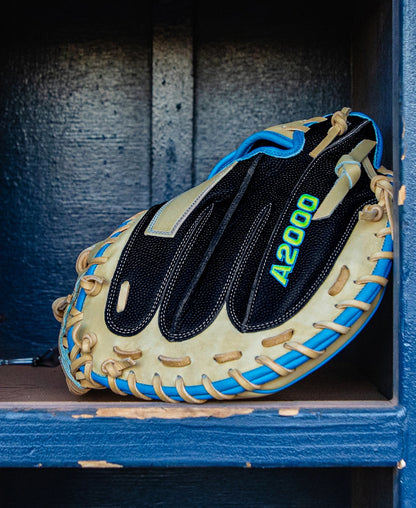 A Wilson A2000 M23SS 33.5″ Baseball Catcher’s Mitt featuring beige and black leather, blue laces, and “A2000” written in green rests on a blue wooden shelf.