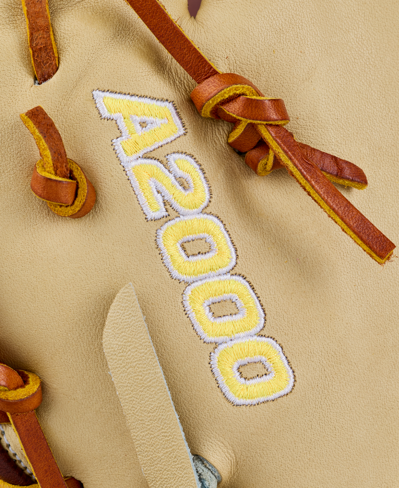 Close-up of the Wilson A2000 1673 13″ Baseball First Base Mitt (WBG06401RT13), a tan leather glove featuring brown leather laces and “A2000” stitched in yellow and white thread on the surface, expertly crafted from durable Pro Stock leather in a 13-inch design.