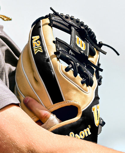 A close-up of a person holding a black and tan Wilson A2K 1786 11.5″ Baseball Glove (model WBG07601RT115), a premium glove from Wilson, with part of their arm and uniform also in view.