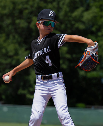 A young baseball player wearing a team uniform and mirrored sunglasses winds up to throw a ball while wearing a Wilson A500 10.5″ Baseball Glove: WBG08401RT105 all-leather youth glove.
