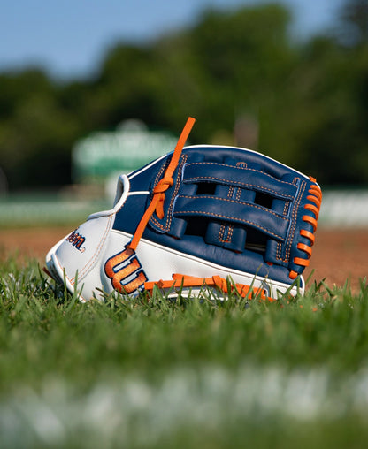 A blue and white Wilson A500 10.5″ Baseball Glove: WBG08401RT105 with orange laces resting in the grass on a baseball field.