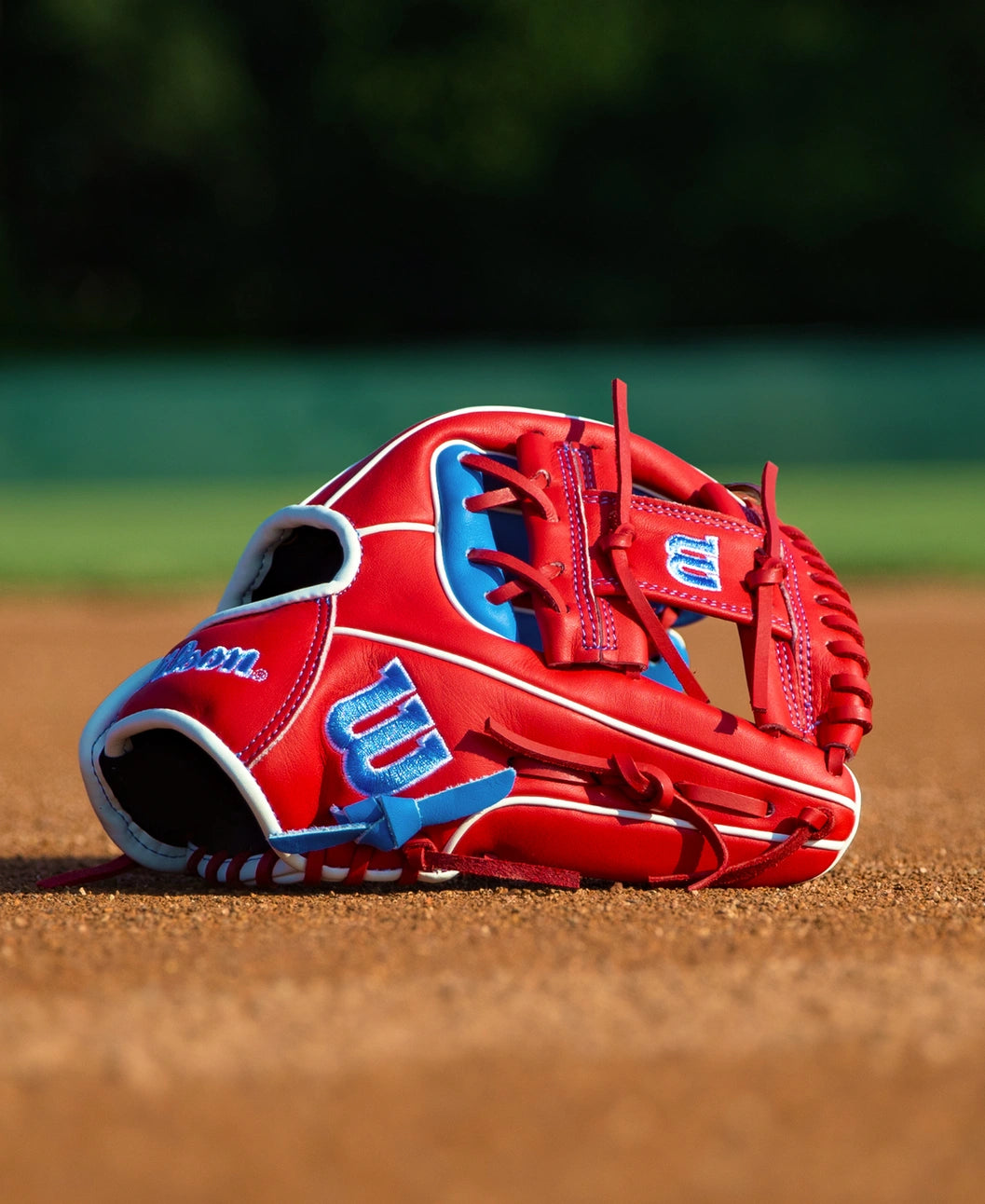 Red and blue Wilson A500 11″ Baseball Glove: WBG08501RT11 resting on a dirt field.