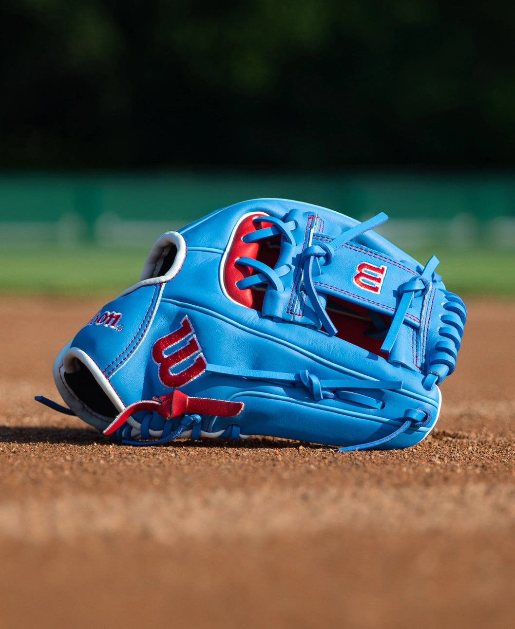 Light blue Wilson A500 11.5″ Baseball Glove: WBG08601RT115 with red accents resting on a dirt field.
