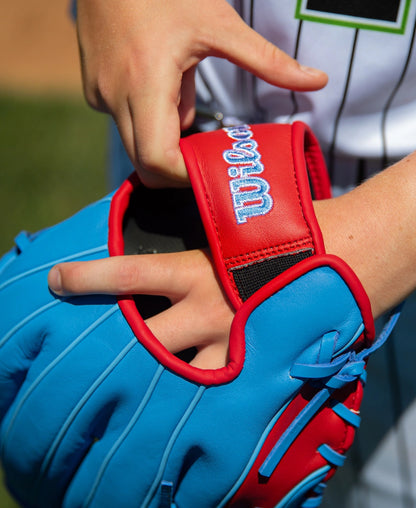 Close-up of a hand adjusting the quick fit wrist strap on a blue and red Wilson A500 11.5″ Baseball Glove: WBG08601RT115.