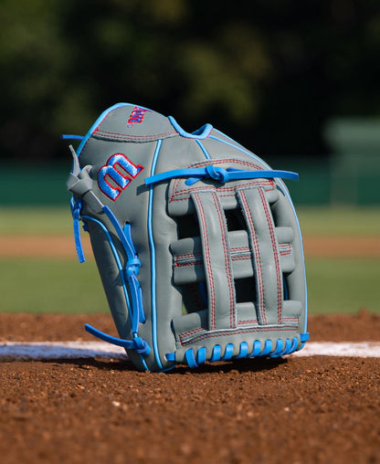 A gray Wilson A500 12″ Baseball Glove: WBG08701RT12 with bright blue lacing, piping, and red stitching on a pitchers mound, featuring a quick fit wrist strap.
