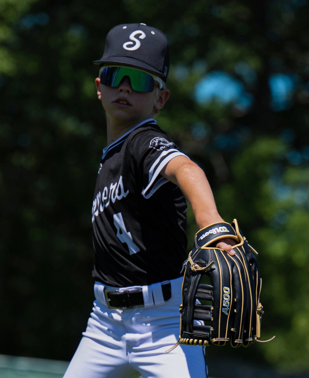 A baseball player wearing a black uniform and mirrored sunglasses holds a black leather Wilson A500 12.5″ Baseball Glove: WBG08801RT125.