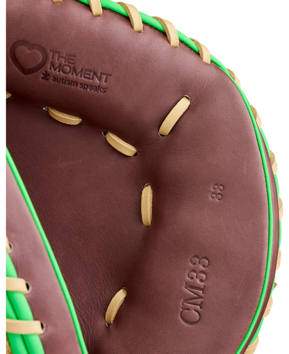 Close-up of a Wilson A1000 CM33 DUBAI 33″ youth baseball catcher’s mitt in brown leather with green trim, tan laces, and embossed text reading “The Moment,” “autism speaks,” and “CM33 33.”.