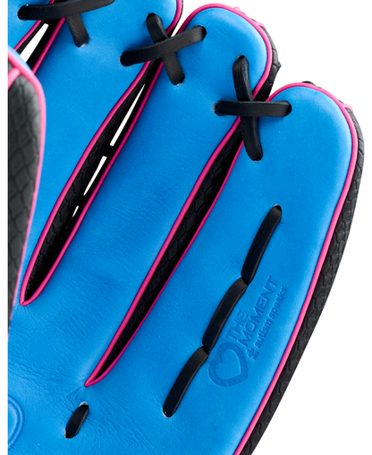 A close-up of a blue Wilson A1000 1922 TUBBS 13″ Slowpitch Glove (WBG25501RT13) with black laces and pink trim, featuring an embossed The Moment logo on the full grain leather.