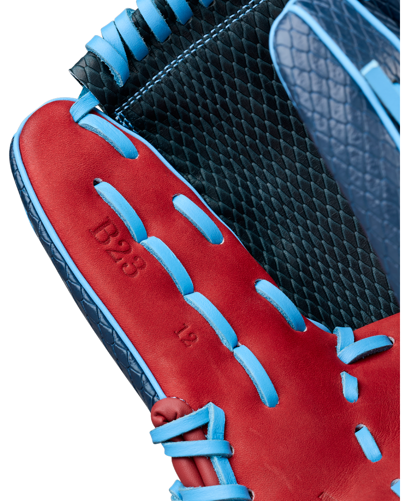 Close-up of a Wilson A1000 B23 GENO 12″ Baseball Glove (WBG26601RT12) by Wilson, showcasing red leather with blue laces and “B23 13” stamped on the palm. The black inner lining features a textured, diamond-shaped pattern, making it an excellent choice for pitchers who want both style and performance.