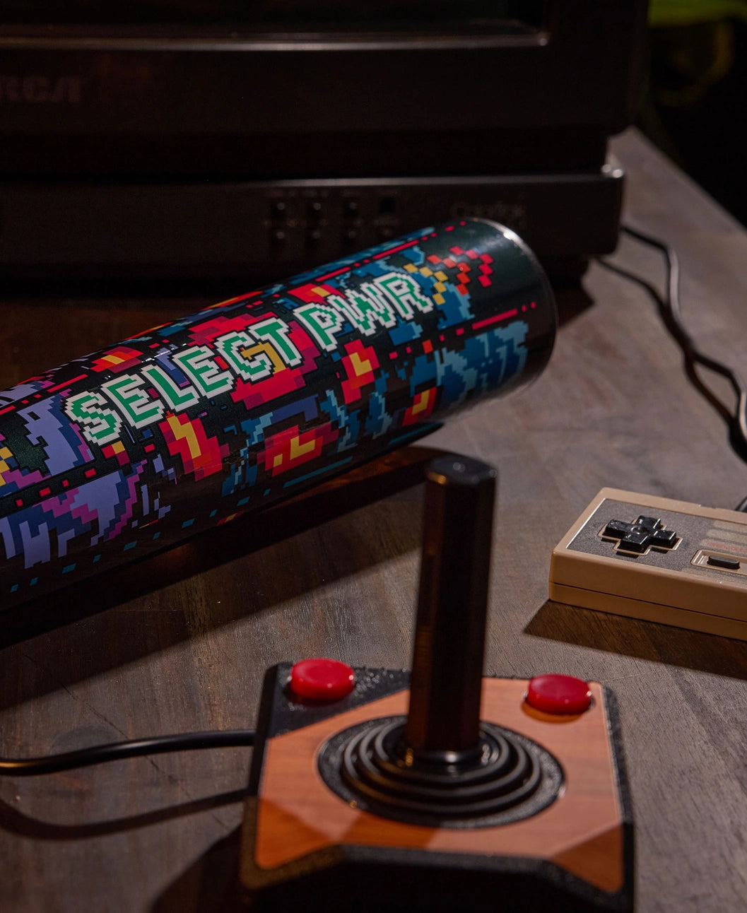 A vintage joystick, a game controller, and the vibrant 2026 Louisville Slugger Select PWR Player 1 (-3) BBCOR Baseball Bat (WBL4182010) by Louisville Slugger rest on a wooden table beside an old RCA TV—nostalgia meets next-gen power gear.