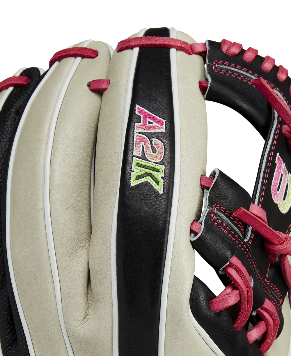 A close-up of the Wilson A2K 1724 11.75" Baseball Glove (GOTM June 2024, WBW1022571175) showcases Pro Stock Select leather in white and black, pink lacing, and "A2K" embroidered in pink, green, and white on a black strip.