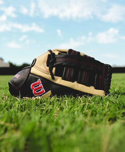 A tan and black Wilson A500 12.5" Baseball Glove (WBW102544125) by Wilson lies on green grass beneath a partly cloudy sky, with a blurred field and distant trees in the background.