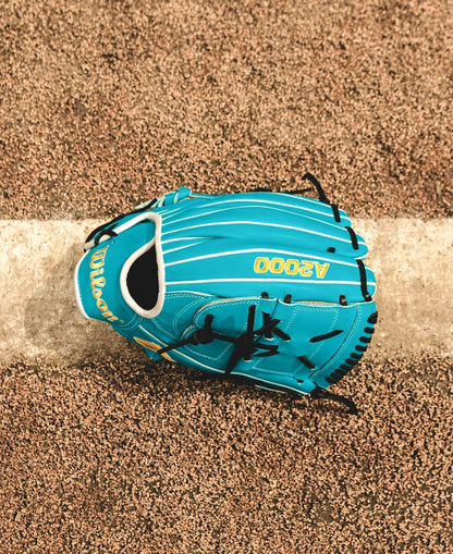 A Wilson A2000 SA17 12" Baseball Glove (WBW10255012), featuring teal Pro Stock® leather and black laces, rests on a brown textured surface across a white line.