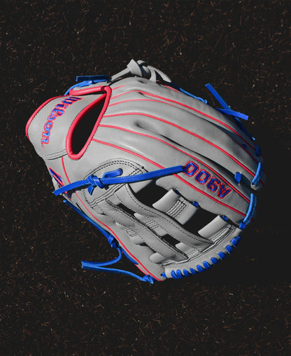 A Wilson A900 PF12 12" Baseball Glove (WBW10257112) in gray with red stitching and blue laces rests on a dark surface, ideal as a youth baseball glove.