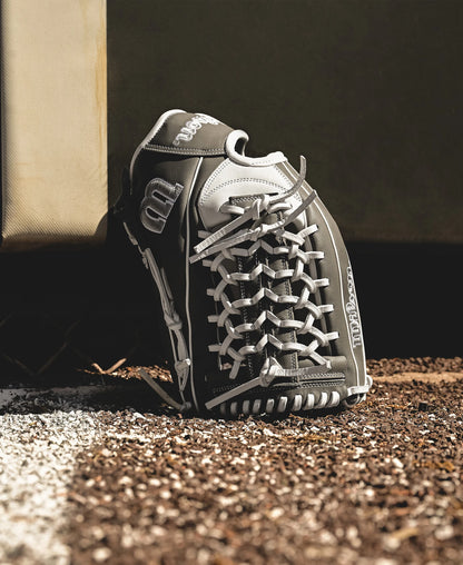 A Wilson A1000 T125 12.5" Fastpitch Glove (WBW102596125) in black and white stands upright against a base on a dirt and gravel field, partly on the white foul line.