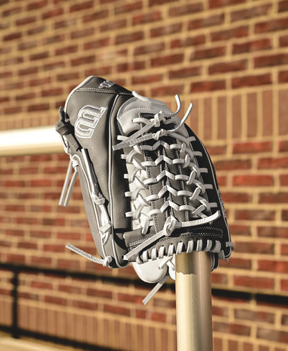The Wilson A1000 T125 12.5" Fastpitch Glove (WBW102596125) by Wilson, in black and white with white laces and full grain leather, rests on a metal pole with a brick wall behind it.