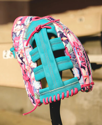 The Wilson A2000 RA56 12.75" Randy Arozarena GM Baseball Glove, featuring a floral pattern with teal and pink laces, rests atop a black bat. This Wilson glove includes SuperSnakeSkin detailing and “A2000” stitching.