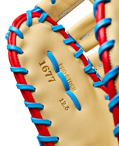 Close-up of the Wilson A2000 1677 12.5" First Base Mitt, featuring tan Pro Stock leather with blue and red lacing, and "1677," "PRO STOCK," and "12.5" stamped in gold on the palm. Model: WBW102753125.