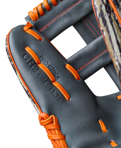 Close-up of the Wilson A2000 GH2 11.75" Gunnar Henderson GM Baseball Glove (WBW1034511175), featuring black leather with orange laces and stitching, embossed "PRO STOCK GH12 GM 11.75" on the palm, and a patterned edge on the left side.
