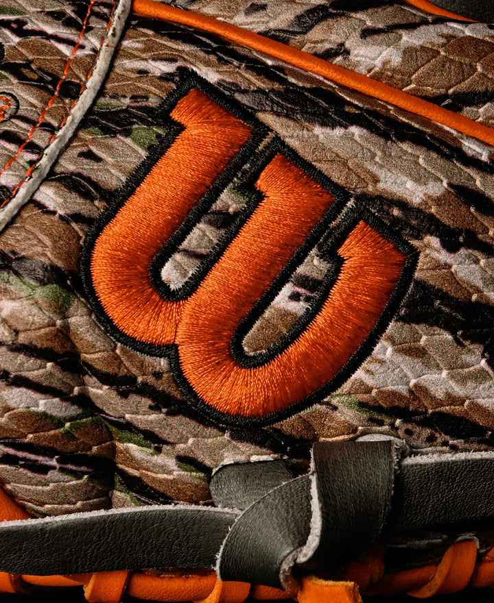 Close-up of a Wilson A2000 GH2 11.75" Gunnar Henderson GM Baseball Glove (WBW1034511175) with a camouflage pattern, orange embroidered W logo, orange stitching, and black and gray leather details.