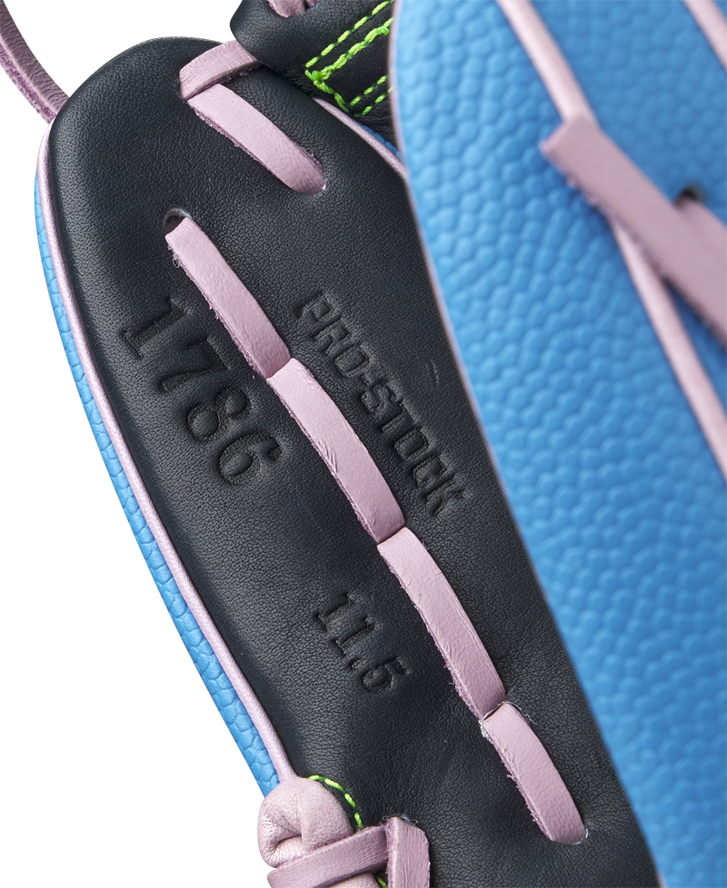 Close-up of the Wilson A2000 1786SS 11.5" GOTM March 2025 baseball glove in blue with black Pro Stock leather, pink lacing, green edge stitching, and embossed text: PRO-STOCK, 1786, and 11.5.