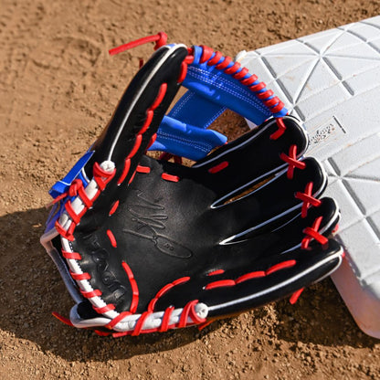 A Wilson A2K MB1175 11.75" Mookie Betts Gameday Baseball Glove (FALL 2025: WBW1035001175), black with red and white laces, crafted from Pro Stock Select leather, sits on brown dirt by a white base on the field.