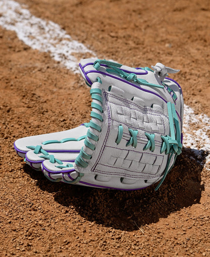 A Wilson A500 Siren 11.75" Fastpitch Glove (WBW1035581175), gray with teal and purple laces and made from top grain leather, lies open on brown infield dirt near a white chalk foul line.