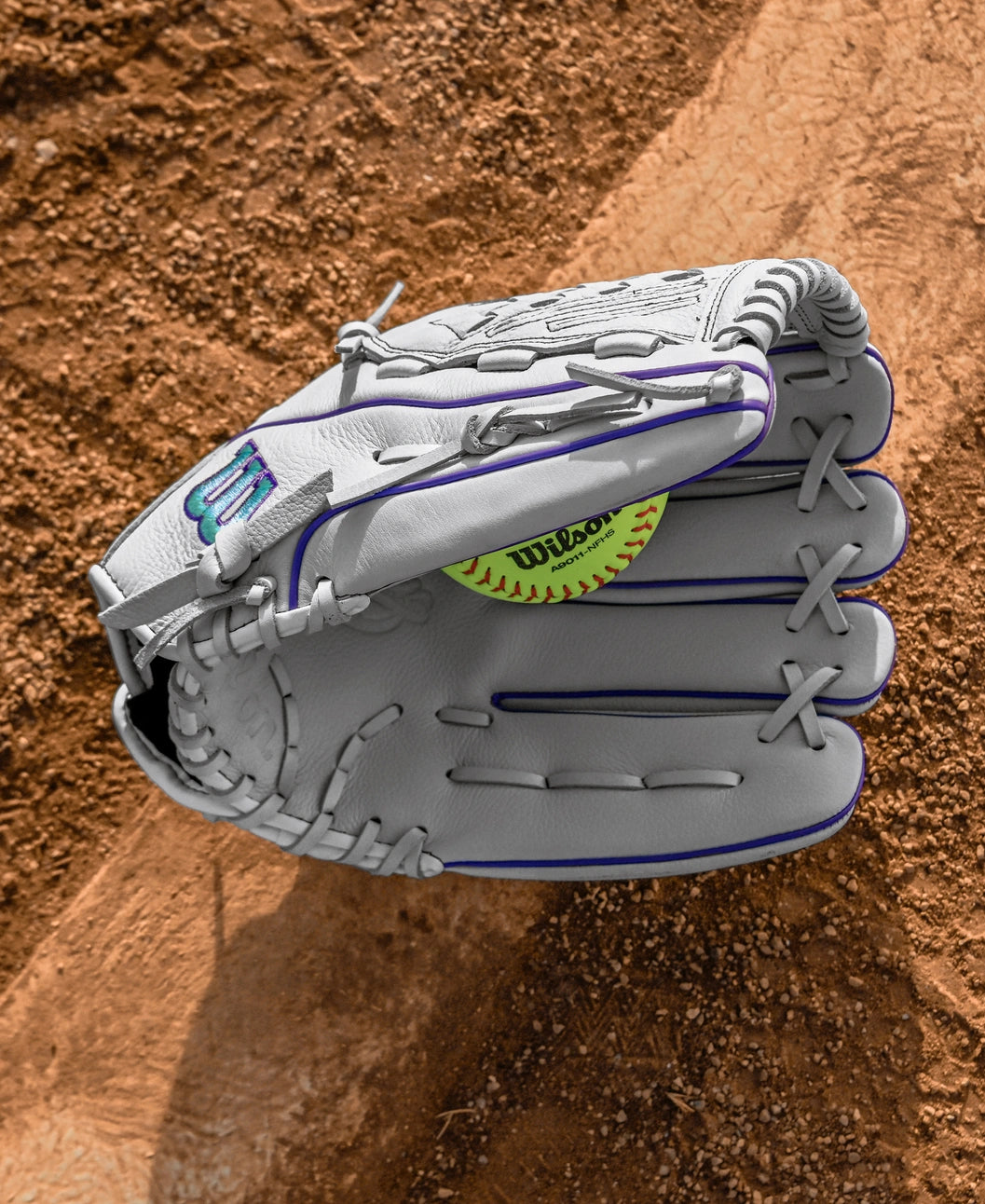 A Wilson A500 Siren 12.5" Fastpitch Glove by Wilson, made of top grain leather, catches a yellow softball on a dirt baseball field.