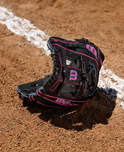 A Wilson A1000 DP15 11.5" Baseball Glove by Wilson in black and pink sits upright on a dirt field next to a white chalk baseline.