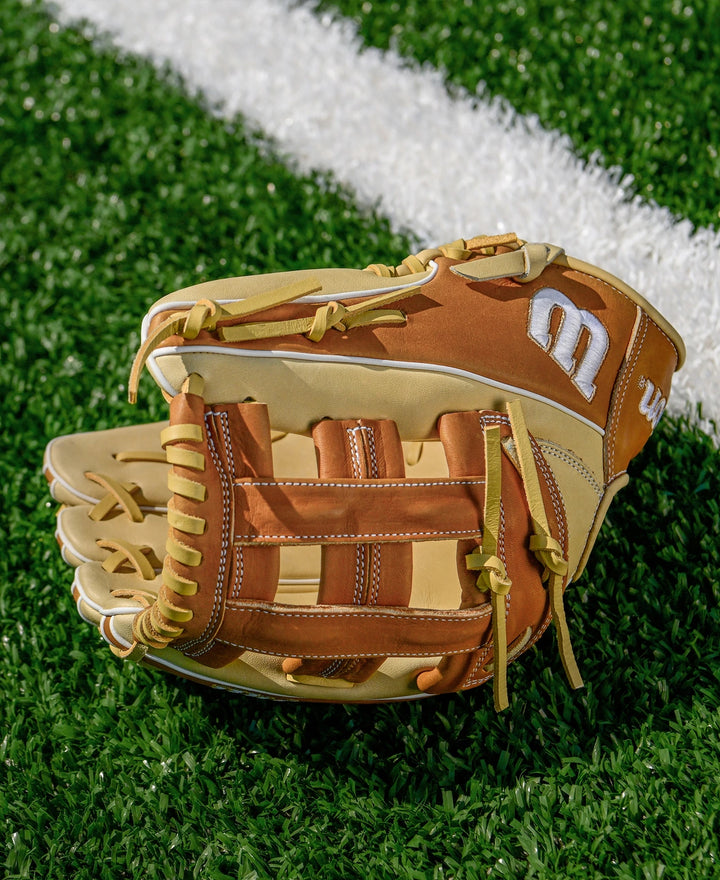 A Wilson A1000 1750 12.5" Baseball Glove (WBW103964125) in brown and tan sits on green artificial turf near a white line.