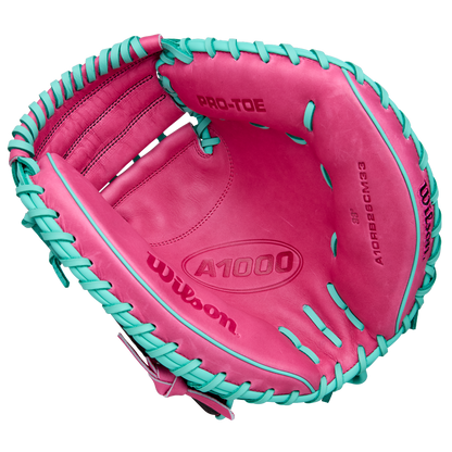A Wilson A1000 CM33 33" Baseball Catcher's Mitt (WBW10396633) in pink with teal laces, seen from above to reveal the palm and interior branding. Crafted from full grain leather by Wilson.