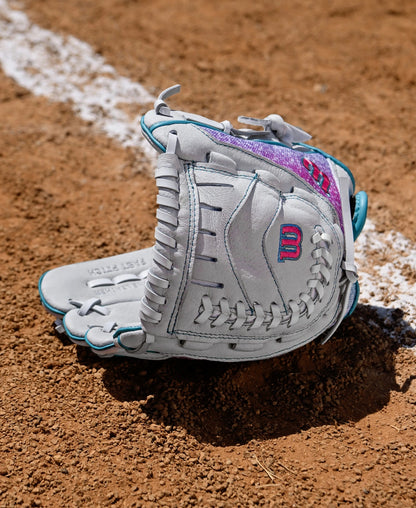 A Wilson Flash 11" Fastpitch Glove: WBW10398411 by Wilson lies open on a dirt field near a white chalk baseline.