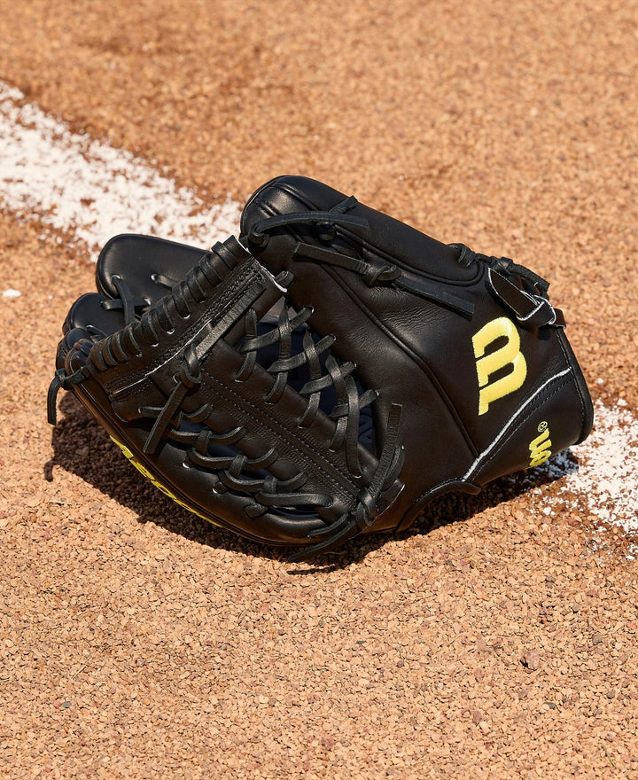 A Wilson A2000 1789 11.5" Baseball Glove (WBW104106115) with yellow lettering rests on the dirt near a white chalk baseline on the baseball field.